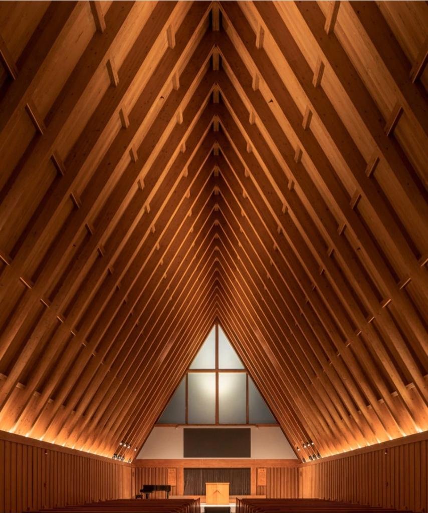 Warm lighting follows the timber beams of a tall institutional interior